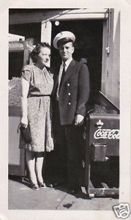 Very Handsome Man in Uniform with Woman and Old Coca Cola Machine